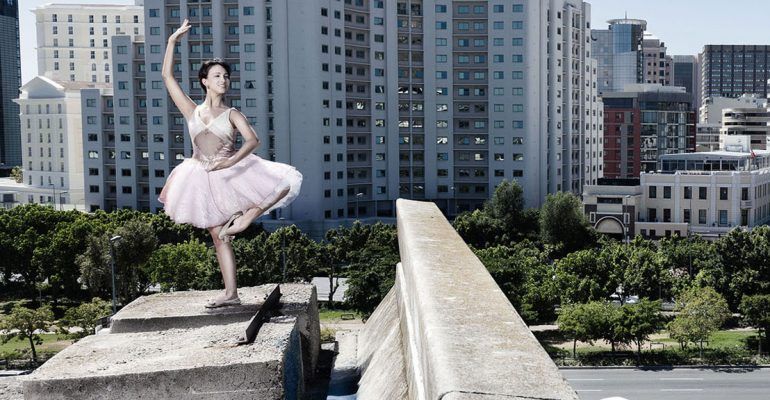 ballerina dancing in front of a city on the edge of a bridge
