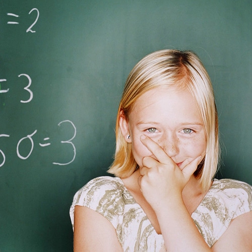 Kleines blondes Mädchen vor einer grünen Schultafel