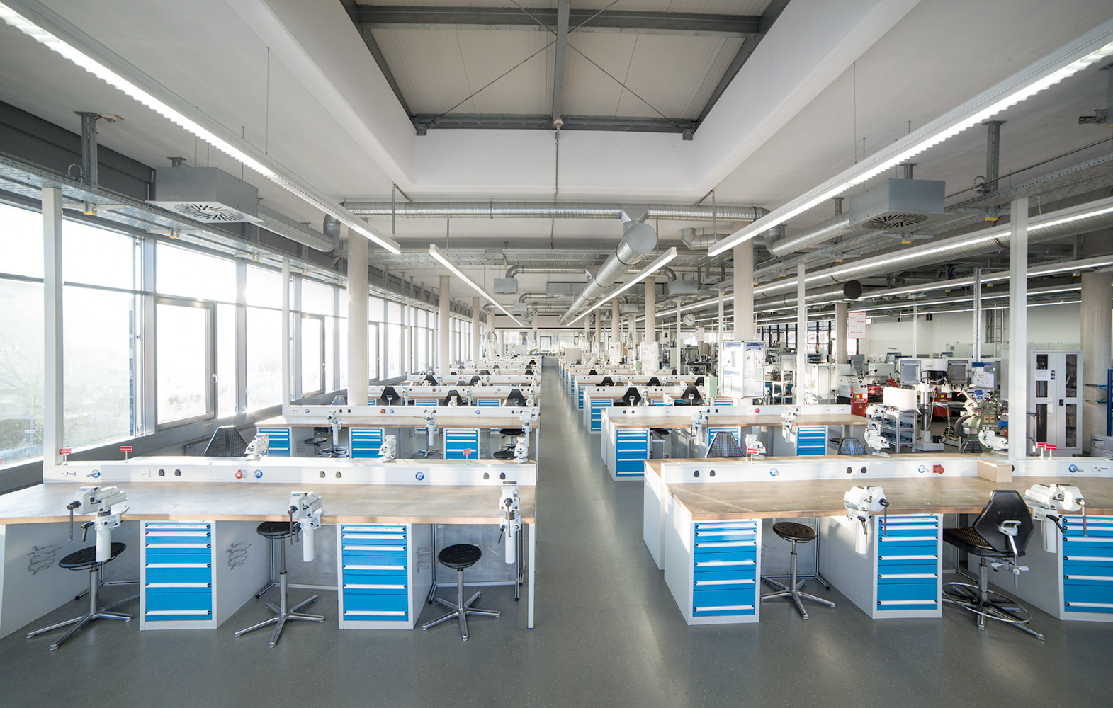 Eine große Halle mit vielen Arbeitsplätzen an langen Werkbänken, die hintereinander aufgereiht sind.
