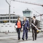 Drei Architekten laufen über den Flughafen in München mit Bauhelmen und dem Twoer im Hintergrund