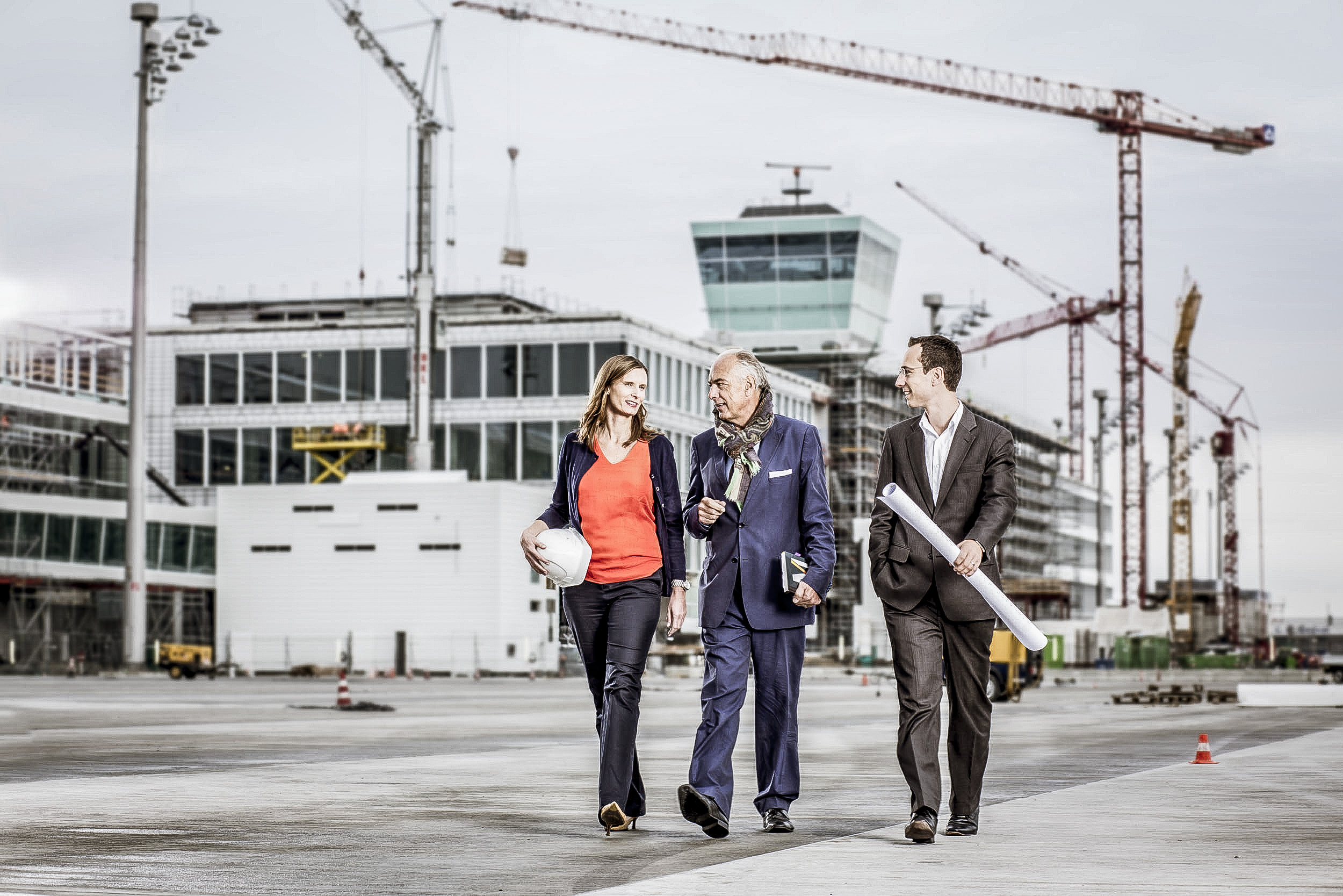 Drei Architekten laufen über den Flughafen in München mit Bauhelmen und dem Twoer im Hintergrund