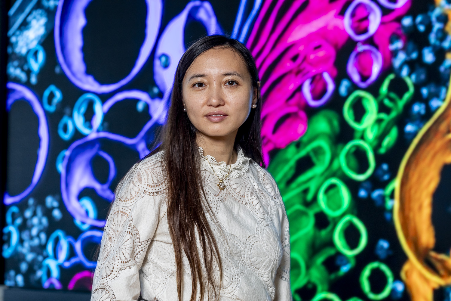 Portrait einer Mikrobiologin mit farbigen zellstrukturen im Hintergrund