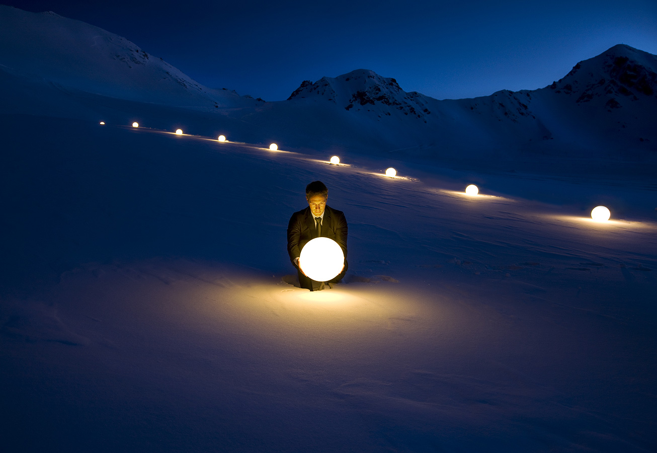 Win Mann sitzt mit einer runden leuchtenden Kugel mitten auf einem schneebedeckten Gletscher während der Dämmerung
