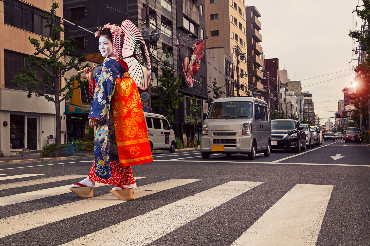 Japanische Meiko, klassisch gekleidet, läuft mit Schirm über eine Strassenkreuzung in Kyoto