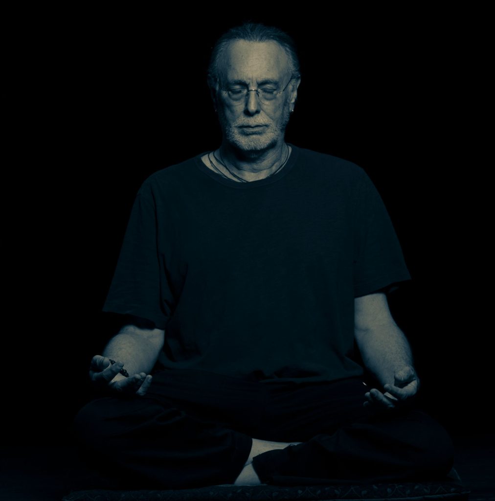 Krishna Das sitzt im Lptussitz mit geschlossenen Augen meditierend.
