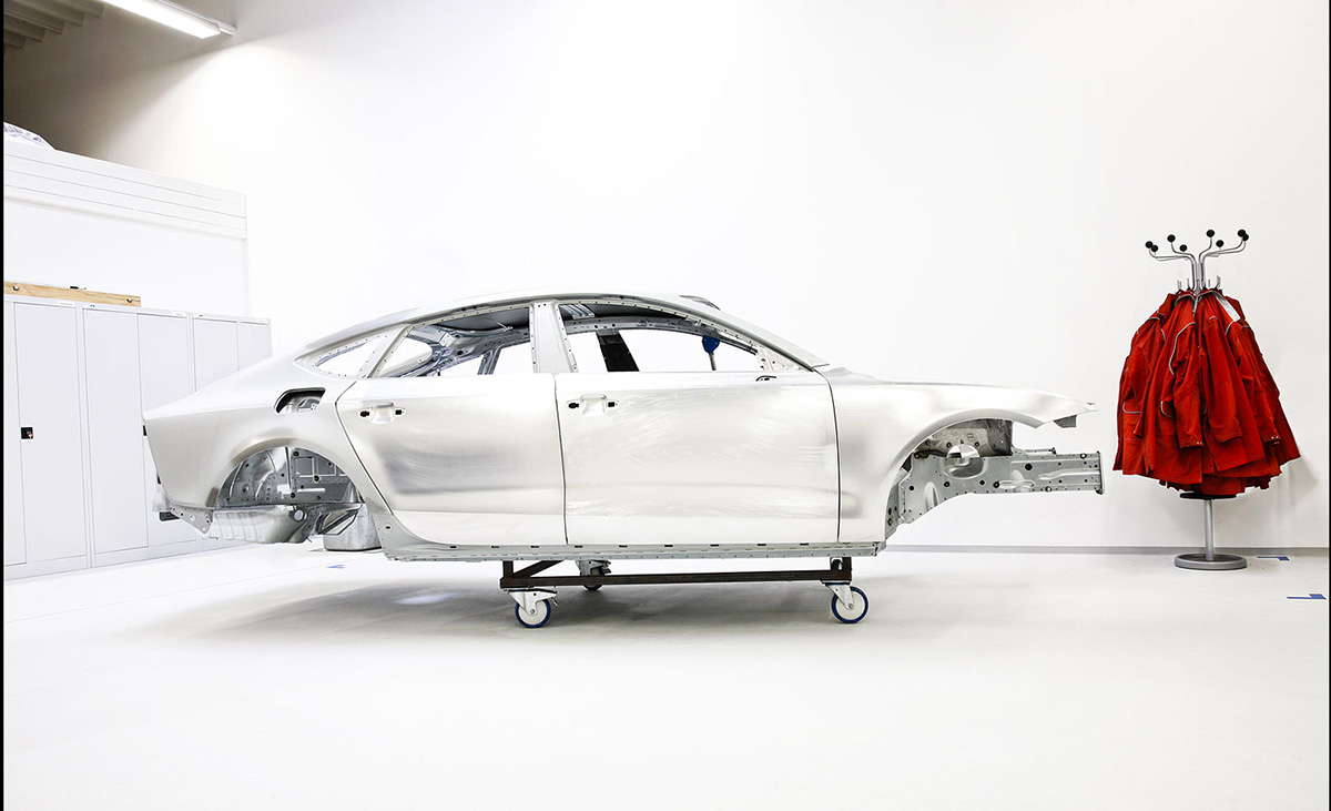 Karosserie eines Audi A5 In der entwichlung, die Karosserie steht auf einem Rollwagen, ist roh das aluminium glänzt in Hintergrund hängen rote Jacken