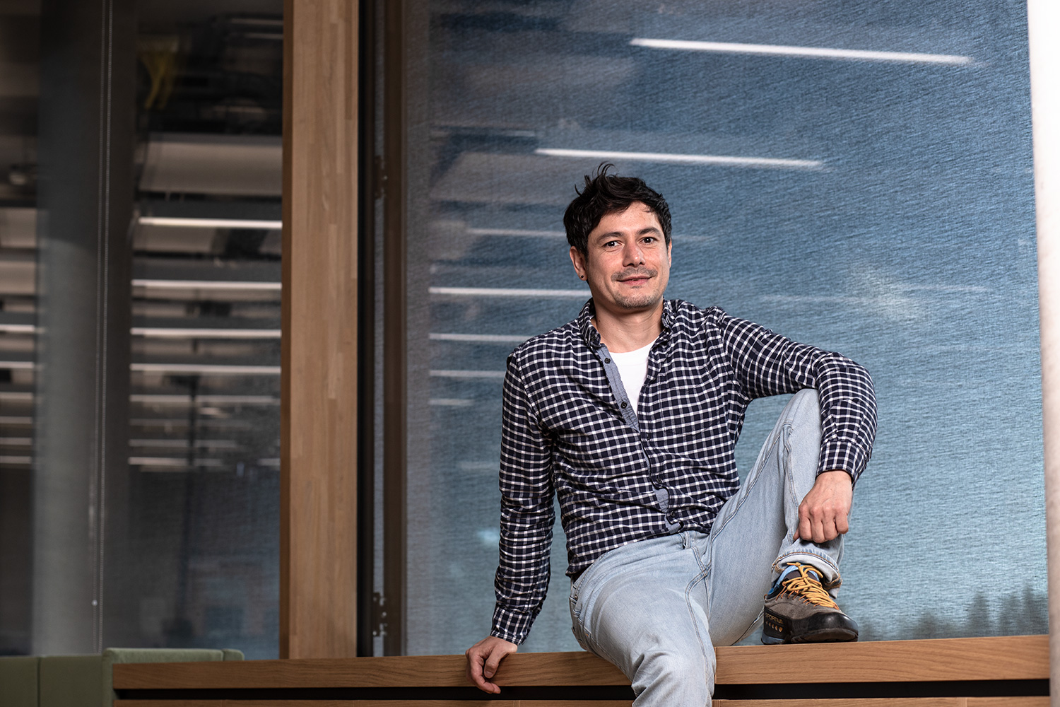 Ein junger Wissenschaftler sitzt bequem auf einem Fensterbrett eines großen Fensters mit einer großen markise und den Refelxen von Lampen im Hintergrund