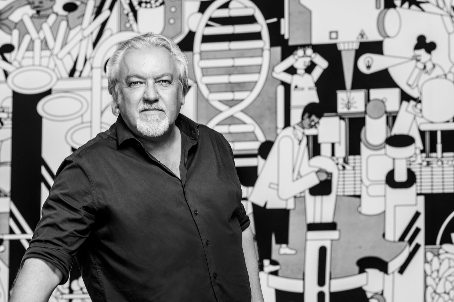 Schwarz Weiss Portrait eines Wissenschaftlers vor einer Comic Wand mit Bildern aus Forschung und Labortechnik und Biologie