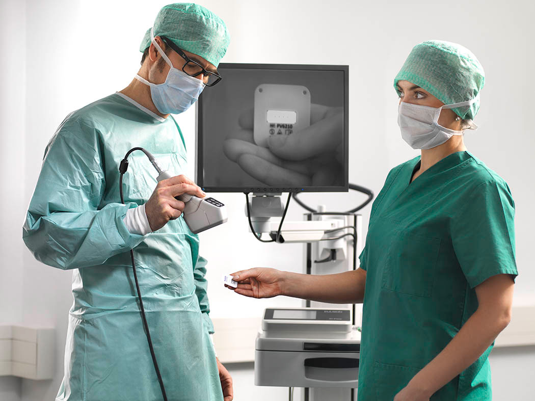 Arzt und Helferin stehen vor einem Diagnosegerät und scannen einen Code ein im Hintergrund sieht man den Bildschirm