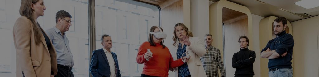 Eine Gruppe von Seminar Teilnehmern die um eine Frau herumstehen die mit einer 3D Brille ausgestattet ist und von der Seminarleiterin angeleitet wird