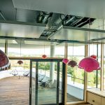 Ausblick von einem Innenraum mit bunten runden Lampenschirmen auf eine Terasse, die Ecke des Gebäudes ist rund