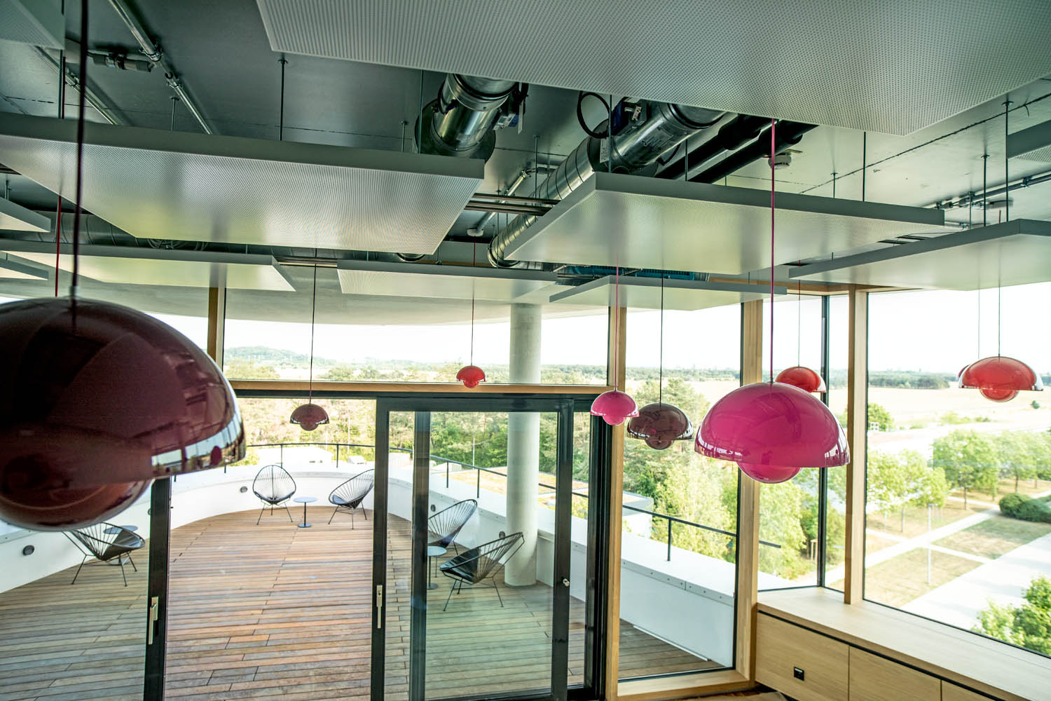 Ausblick von einem Innenraum mit bunten runden Lampenschirmen auf eine Terasse, die Ecke des Gebäudes ist rund