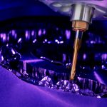 Eine Fräsmaschine arbeitet sich durch eine Zirkonronde im close up bunt fotografiert mit lila licht und gelben bohrer