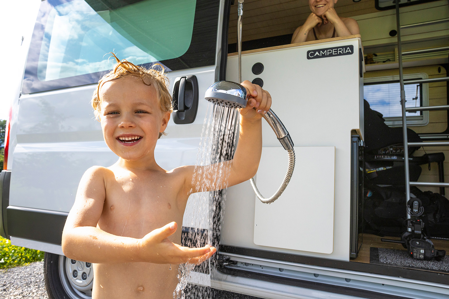 Ein kleiner Junge steht vor einem Campingfahrzeug und probiert die Dusche aus
