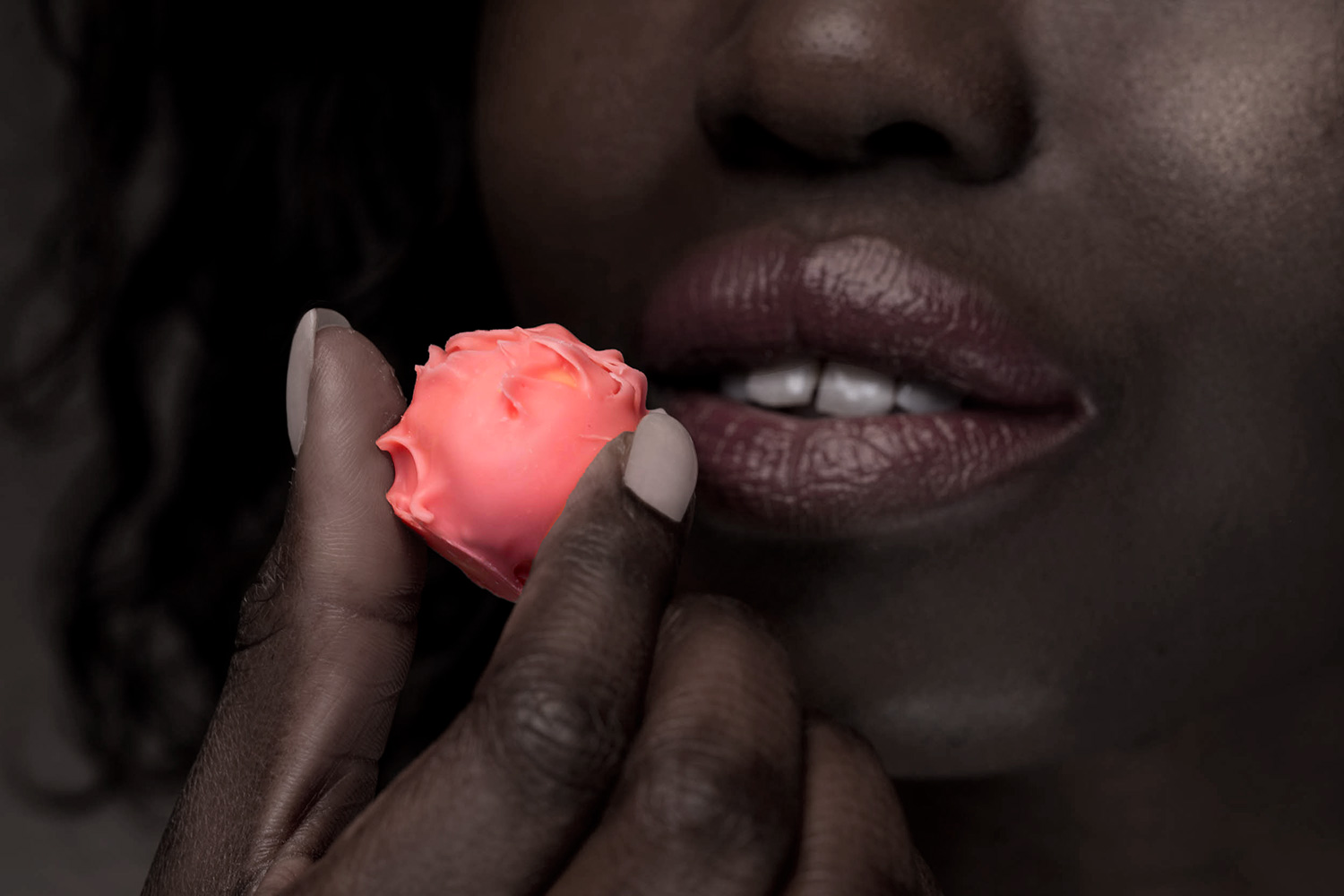 eine rosa Praline vor einem Mund einer schwarzen Frau