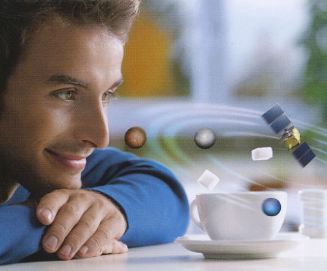Ein junger Mann schaut über einen Tisch auf seine Kaffeetasse und beobachtet darüber fliegende Sterne und Satelliten